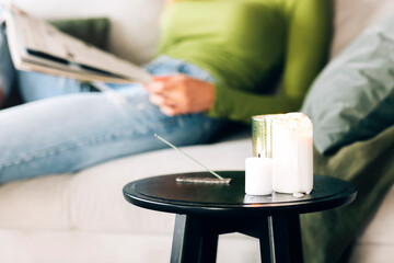 Burning aroma stick and candles on coffee table over blurred background of living room