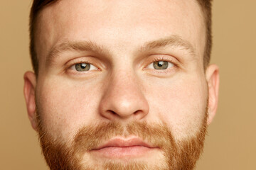 Obraz premium Headshot. Close up portrait of attractive young man with bear, well kept, smooth skin against beige studio background. Concept of beauty treatment, selfcare and hygiene, cosmetic, spa. Ad