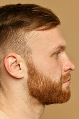 Obraz premium Half face close up portrait of young attractive man with red hair and beard against beige studio background. Male facial care routine. Concept of beauty treatment, selfcare and hygiene, cosmetic, spa.
