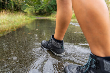 Close up of legs of hikers with boots stepping on a puddle to cross the small path in the middle of nature on the trekking day
