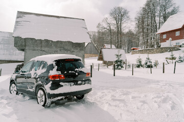 Snow-covered black SUV stands near a cottage in a small village