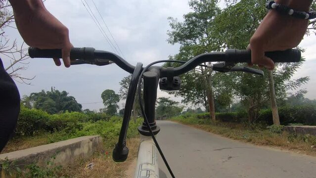 Cycling with peace on road of village in Assam surrounded with fields and trees.