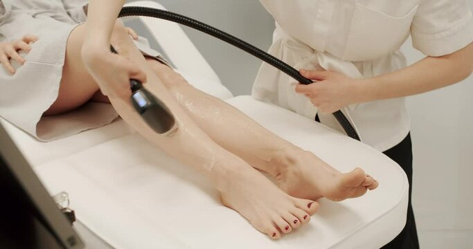 Beautician removes hair on beautiful female legs using a laser. Hardware removal of hair on the legs in a beauty salon. Female beautician doing laser hair removal on slim legs of beautiful young woman