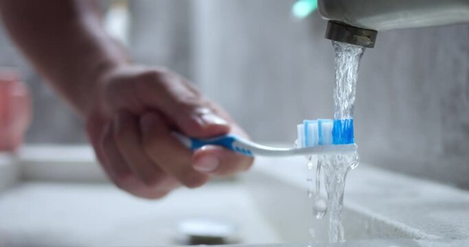 Hand rinsing toothbrush under water. Man wets bristles of toothbrush under running water to soften bristles for more comfortable easier brushing process. Close Up, Slow Motion. Teeth brushing concept