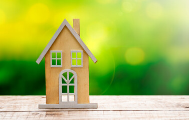 Wooden house model on wooden table with defocused green grass at background. Copy space