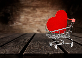 Wooden Red heart in mini grocery cart on wooden table. Copy Space
