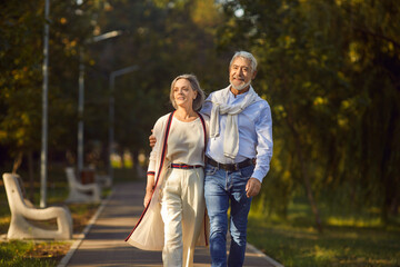 Happy smiling senior couple family hugging while walking in summer city park enjoying retirement...
