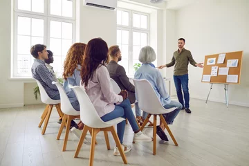 Fototapeten Business coach making a presentation for a diverse audience in an office workplace. Young man sharing his professional experience with a team of corporate workers during a business training meeting © Studio Romantic