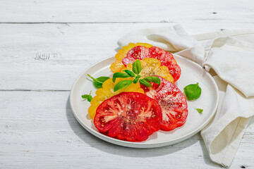 Colorful Heirloom tomato harvest. Ripe ribbed vegetables with fresh basil leaves. Wooden background