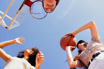 Stylish cool teen girls gathering at basketball court, friends playing basketball outdoors