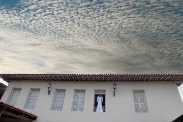 Vestido de noiva pendurado em uma parede branca com fundo de céu azul

