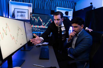 Two stock investors discussing and pointing interesting market stock on monitor. Trend of the...