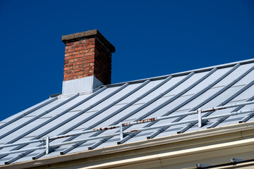 An old red brick chimey on a metal roof with ice breaker