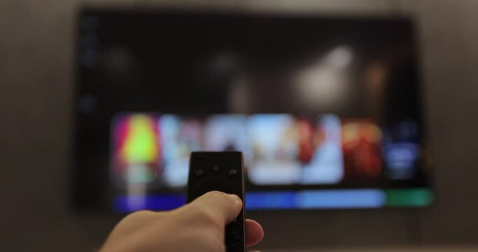 Man hand selects tv channels with remote control at living room on sofa. Man controls TV using a modern remote control. Close up view.