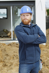 confident young builder posing with folded arms outdoors