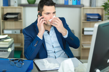 man at work in office blowing his nose with tissue