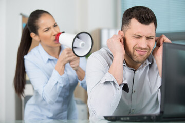 woman shouting through megaphone at male colleague in office
