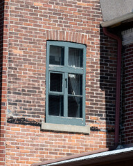 A damaged wooden window frame in a red brick wall