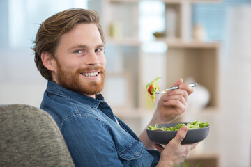 man laid on the sofa eating a salad