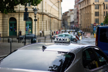 Sign taxi on the car roof that is parked next to cross road in European city. Selective focus,...