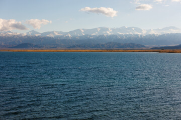 Obraz premium Blue calm water in Issyk-Kul lake with mountains on background at autumn afternoon.
