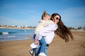 Rear view of a happy mother giving piggyback ride to her lovely daughter at beach.