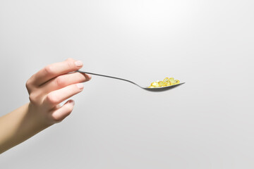 hand holding spoon with yellow fish oil pills on gray background - obrazy, fototapety, plakaty