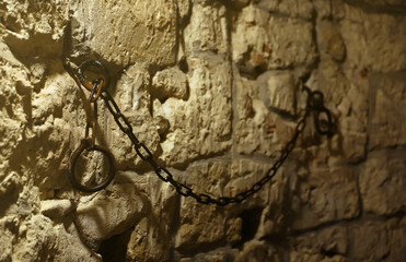 Slavery and bondage strong steel old shackles on stone wall in castle cellar or tomb