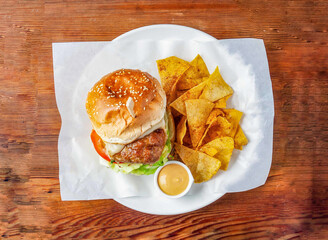 classic chicken burger with cucumber, tomato and cabbage, mayonnaise dip and crackers served in dish isolated on wooden table top view of hong kong food