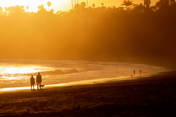 A couple walks their dog, while children play in the distance on a beach in Santa Barbara, California