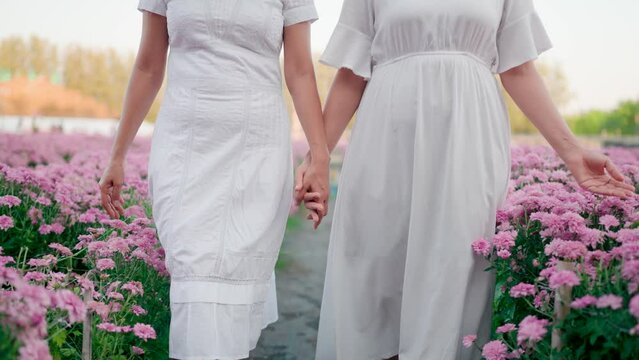 Girl and friend holding hands walking in pink flower garden