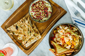 Shrimp pasta dish with hummus and pita in the background, overhead