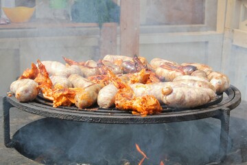 Fried sausages and chicken wings on barbecue grill in the village. Frying meat on open fire. Barbecue party on backyard of country house cabin. Street food festival. Home cooking outdoor. Picnic time