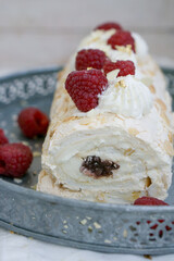 Homemade Mringue Pavlova roll cake with whipped cream and fresh raspberries on top close up selective focus