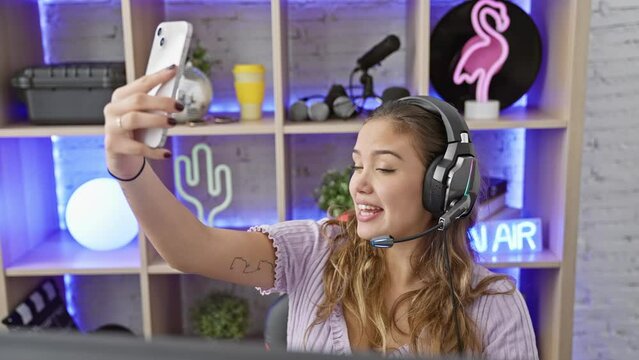 Gaming vibes, beautiful young hispanic woman streamer smiling and engaging in chatty video call from home's gaming room, mastering technology while playing