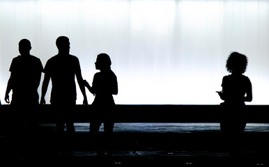 Blurry silhouettes of three young friends and a boy is looking at a girl standing alone