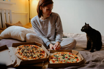 lonely woman at home with a cat ordered two pizzas. Eating pizza in bed at home.