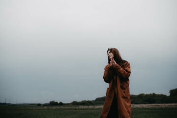 fashionable woman in a brown coat in a field, loneliness and gloom