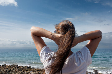 A calming and contemplative moment of self-care in nature with a confident woman watching the dreamy ocean sky on a wellness vacation