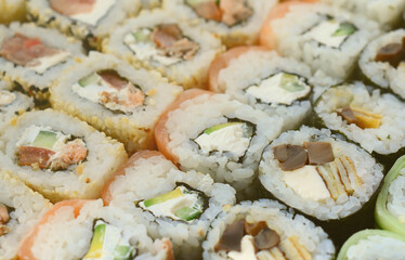 Close-up of a lot of sushi rolls with different fillings lie on a wooden surface. Macro shot of cooked classic Japanese food with a copy space.