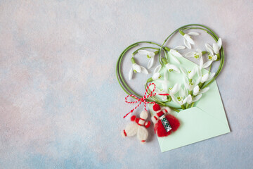 Decorative background with snowdrop flowers in the shape of a heart in an envelope and a symbol of the March 1 holiday Martisor, copy space.