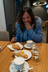 beautiful middle aged woman having breakfast shows surprise at the beauty of the croissants