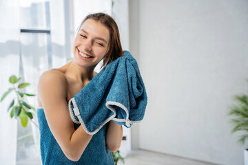 Happy blonde woman drying wet hair with cotton towel in bathroom. Front view of beautiful caucasian...