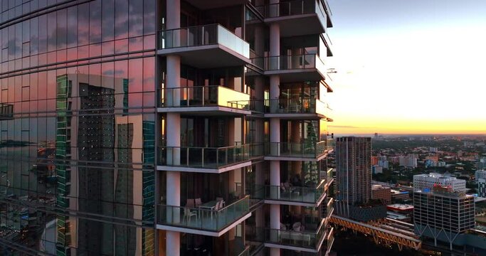 Flying around the luxurious modern high-rise building with windows reflecting light at sunset. Block of flats in Miami, Florida, USA.