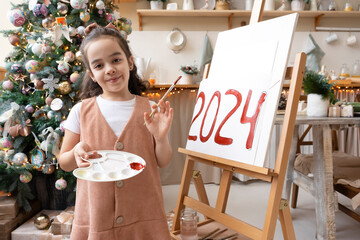 Talented schoolgirl artist paints red numbers 2024 on easel with palette and brush. Christmas tree...