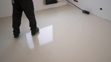 A worker applies gray epoxy resin to a new floor. A worker with a needle roller applies a new...