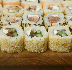 Close-up of a lot of sushi rolls with different fillings lie on a wooden surface. Macro shot of cooked classic Japanese food with a copy space.