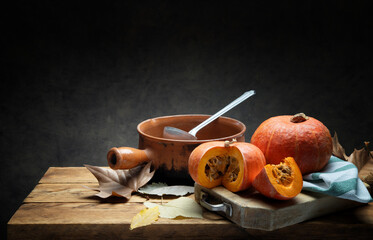 Pumpkins on rustic wooden table with old terracotta pan, dry leaves and dark gray background, space...