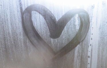 A heart-shaped drawing drawn by a finger on a misted glass in rainy weather
