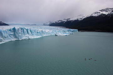 People kayaking on a lake next to an imposing glacier. Perito Moreno Glacier, Calafate, Argentina. 